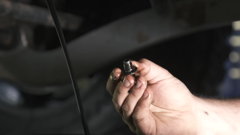 A Person Holding a Car’s Oil Drain Plug with Oil Stains on Their Fingers