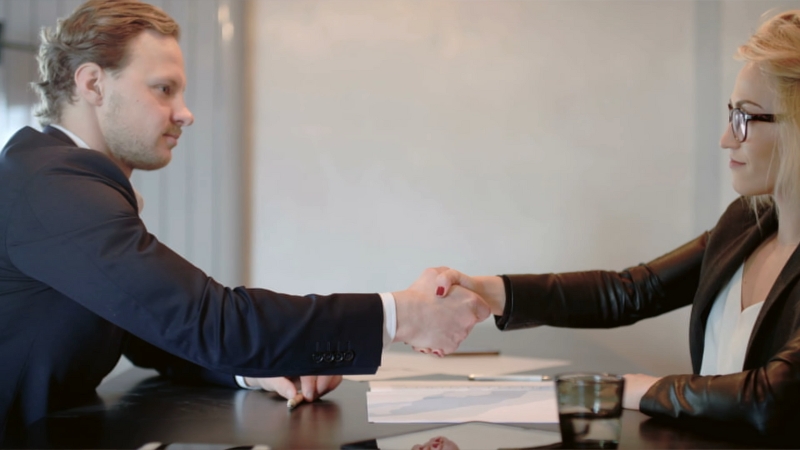 Two People Shaking Hands Across a Table, Finalizing an Agreement