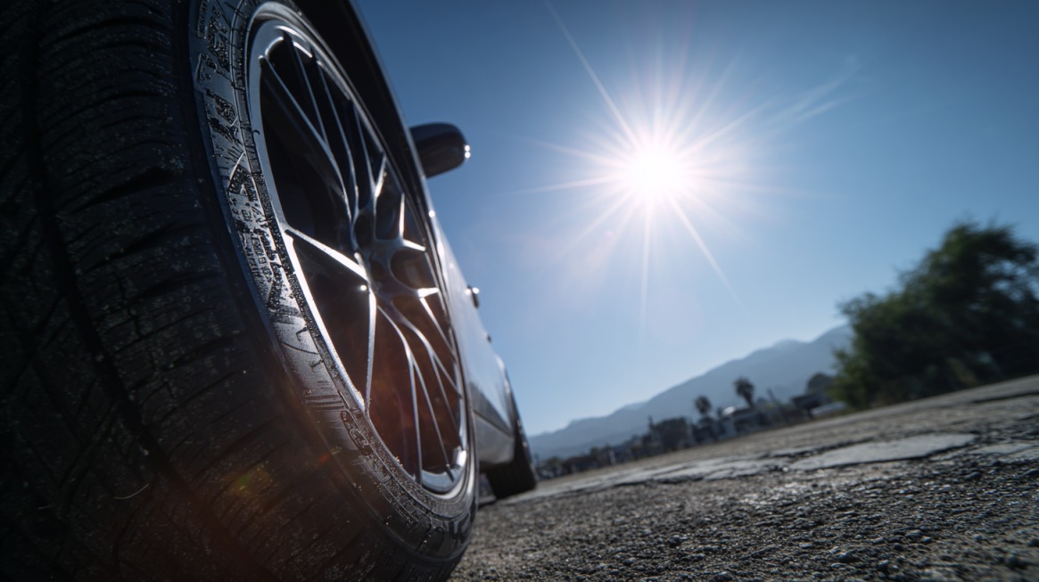 Low-angle view of a car tire on a sunny day with the sun shining brightly in the sky