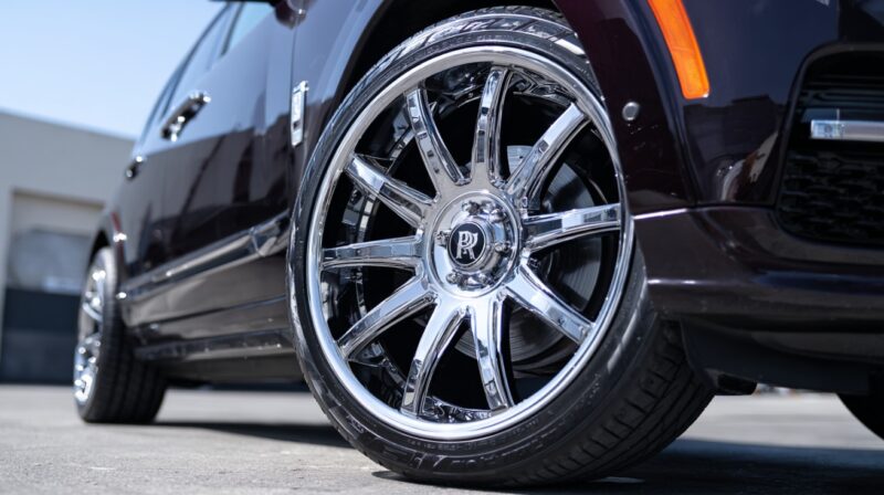 Close-up of a luxury car’s shiny chrome wheel with Lexani tires, reflecting sunlight on a smooth pavement background