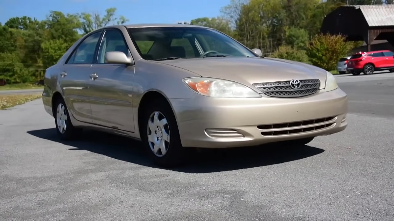 Beige early 2000s Toyota Camry parked on a paved street near trees