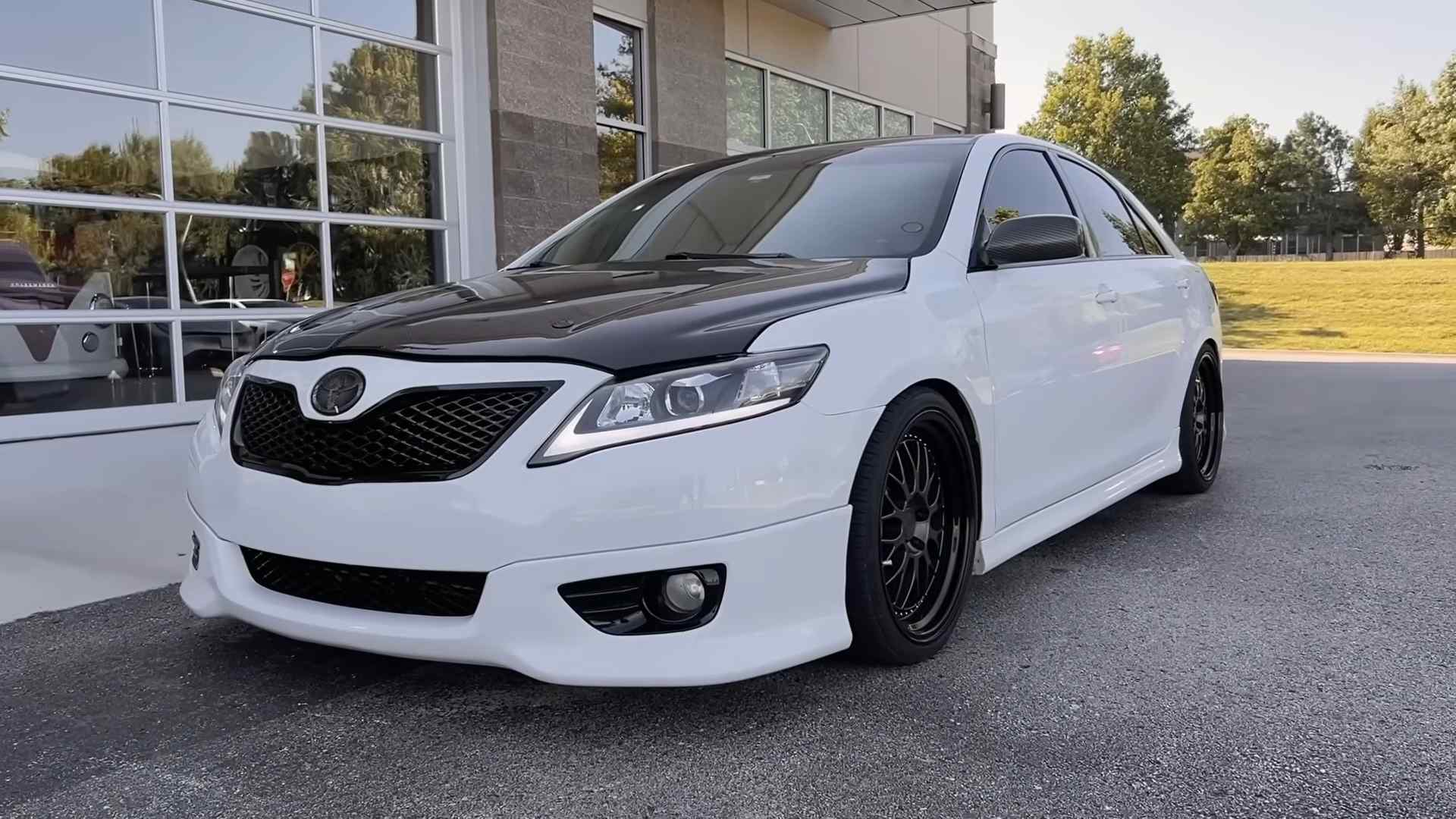 White Toyota Camry with black hood and custom wheels parked outside a building
