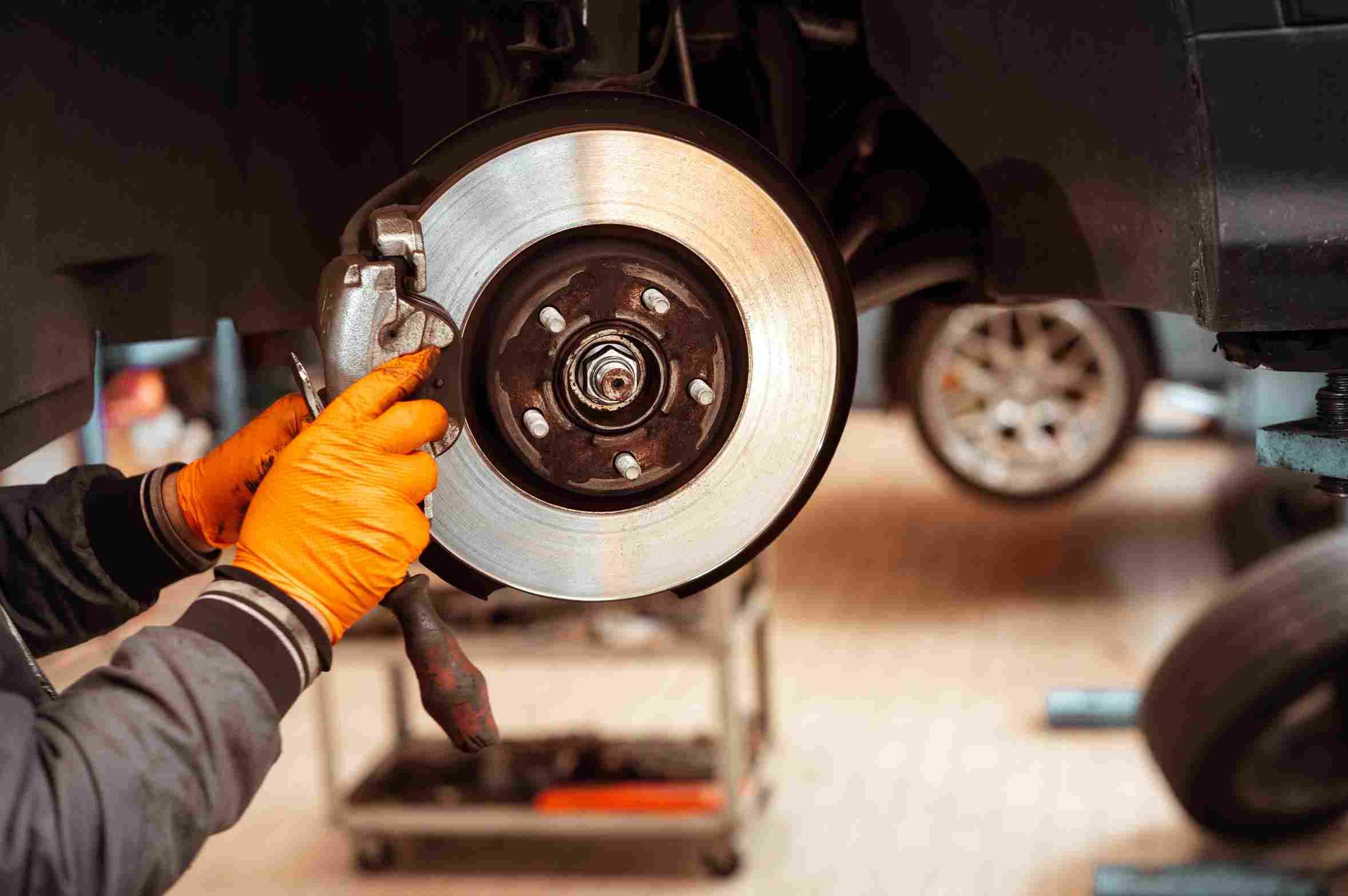 Mechanic wearing gloves working on a car brake rotor and caliper while the vehicle is lifted