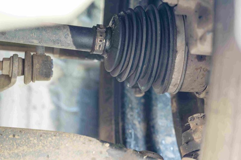 Detailed view of a car CV joint with rubber boot and axle showing wear and grease