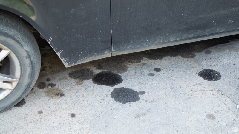 Dark fluid spots on the ground under a parked car near the front wheel