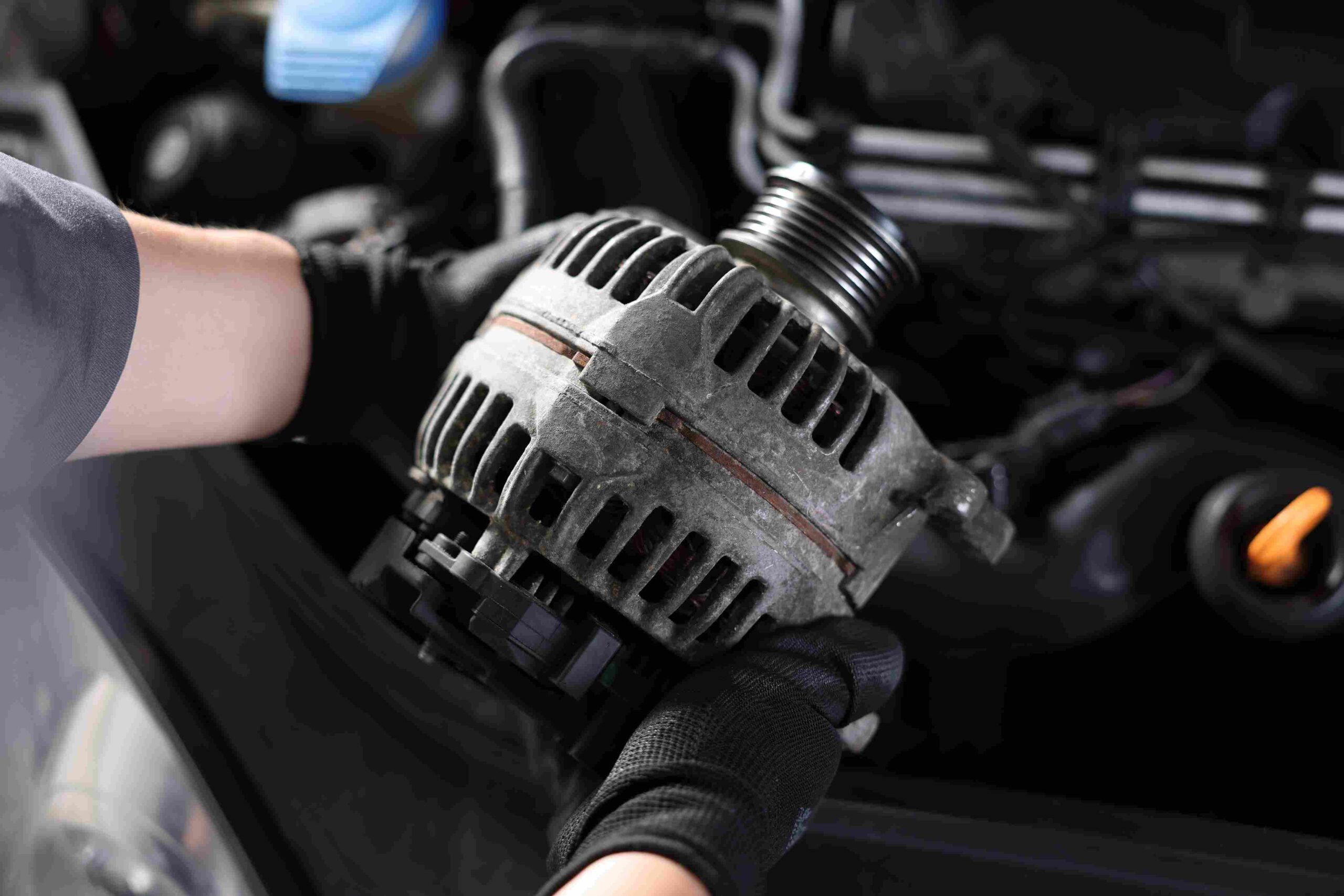 A person holding a car alternator near an engine bay