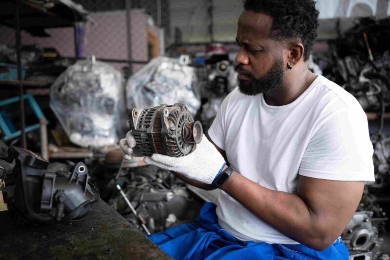 A mechanic holding and examining a car alternator in a workshop