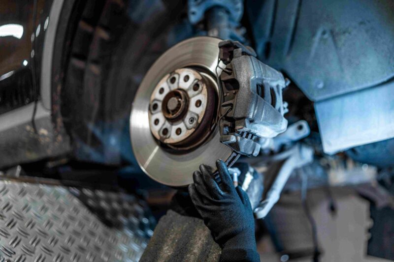 Close up of a brake rotor and caliper with a mechanic’s gloved hand working on the car