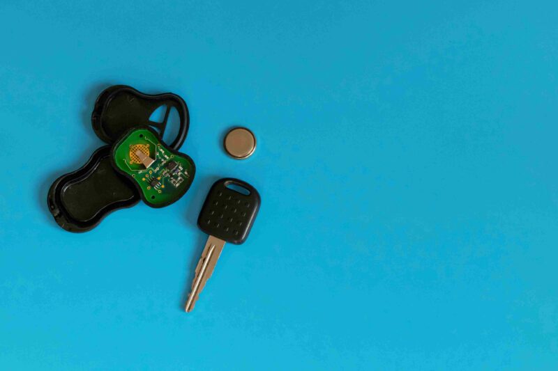 Opened car key fob with internal circuit board and a small coin battery beside a car key