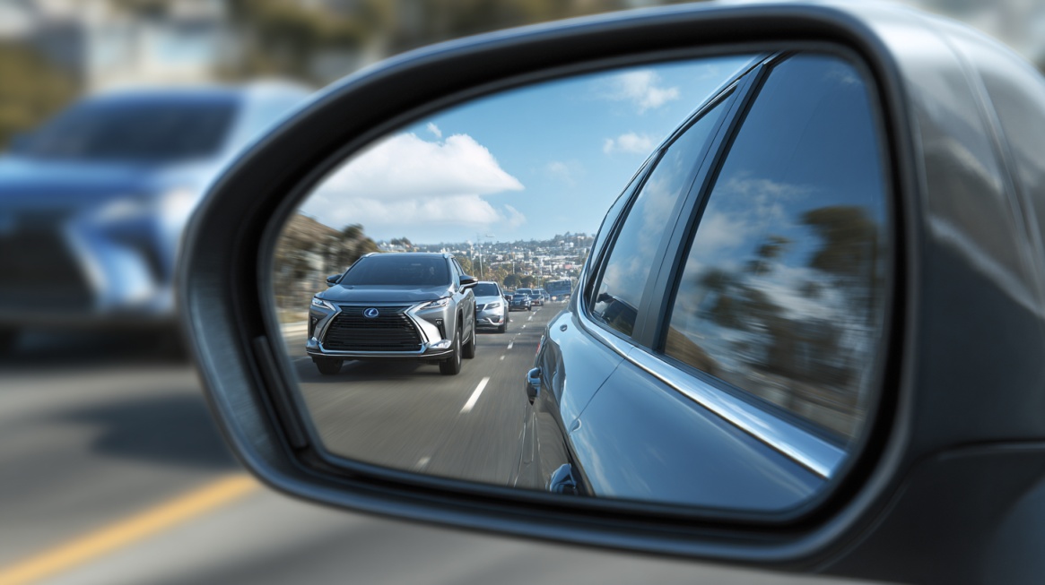 Side mirror view showing a car approaching from behind on a multi-lane road