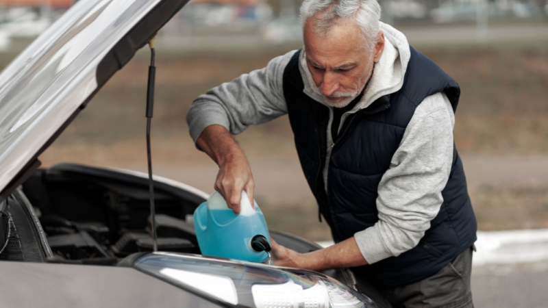 Man adding coolant to a car engine with the hood open