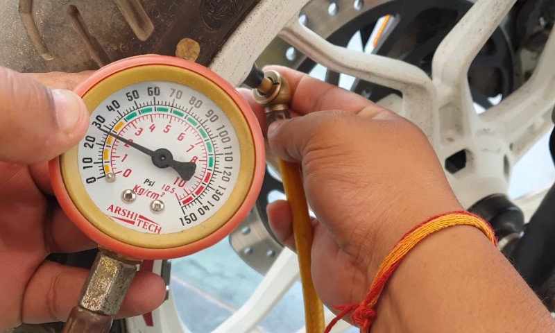 Hands using a pressure gauge with a red and yellow dial to check tire pressure