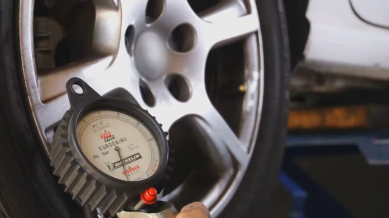 Gauge checking low tire pressure on a car tire near the wheel rim