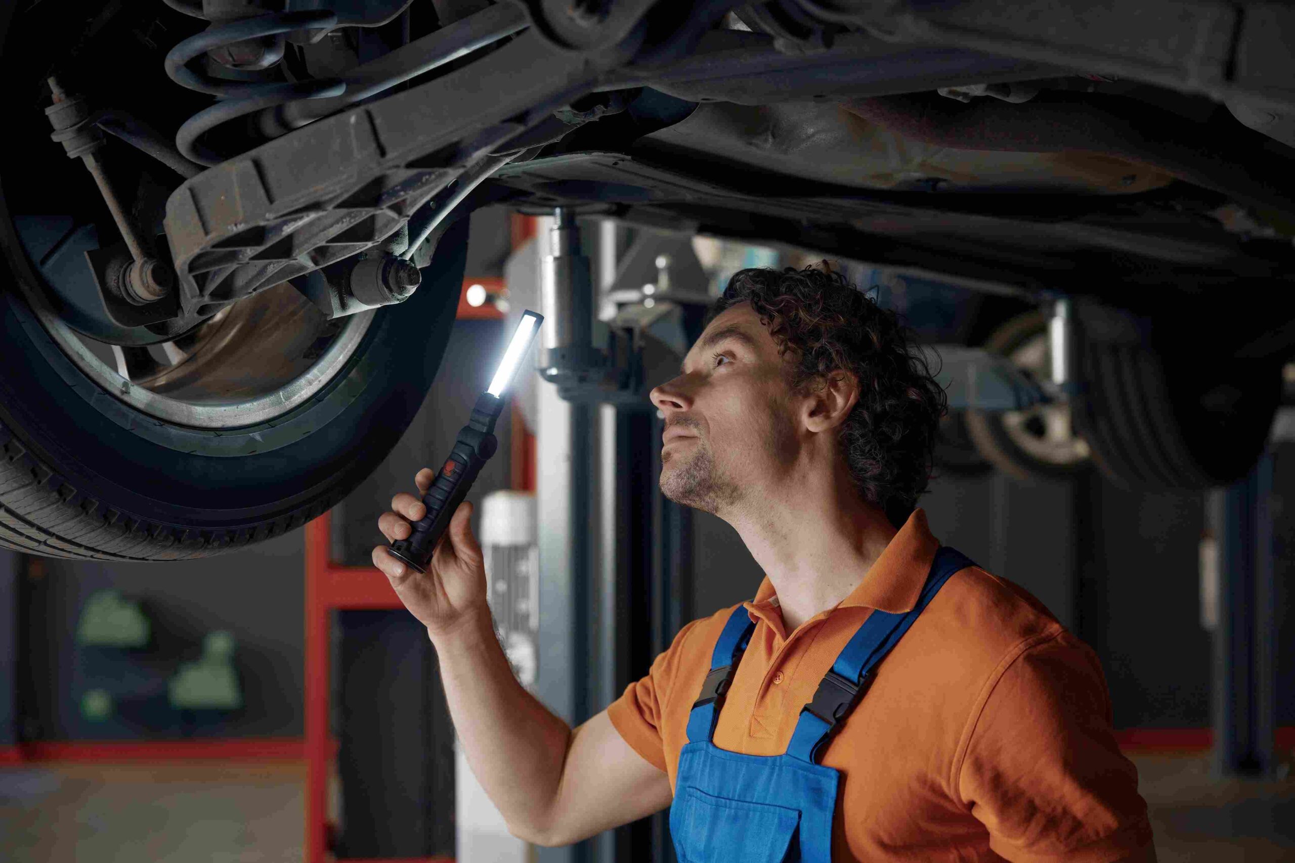 Auto technician holding a flashlight while examining a vehicle on a lift from below