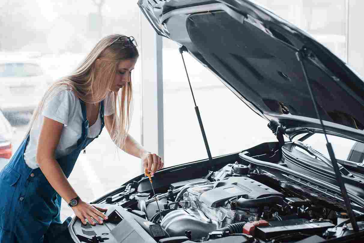 Person inspecting a car engine under the open hood during vehicle maintenance