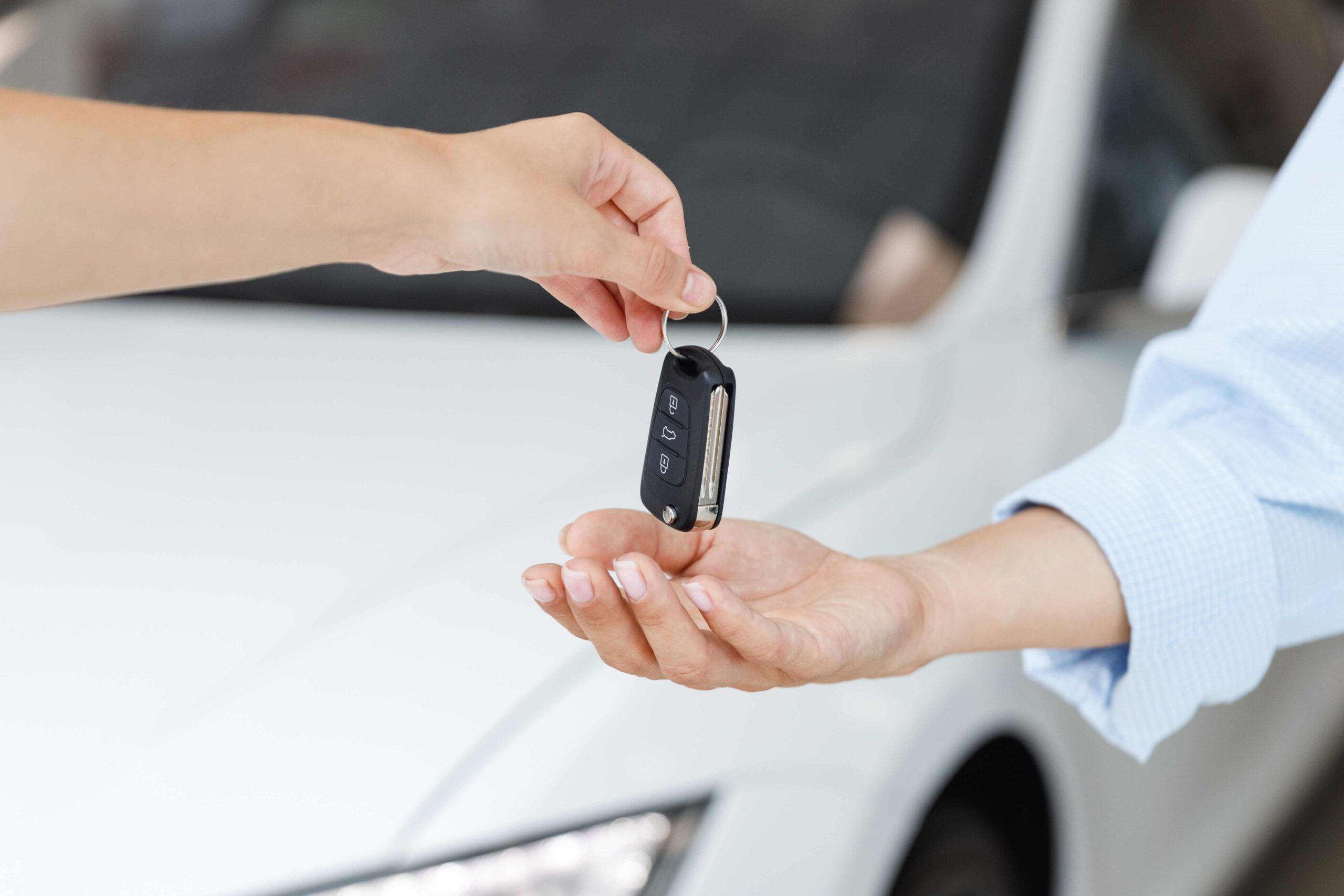 Person handing a car key fob to another person beside a car