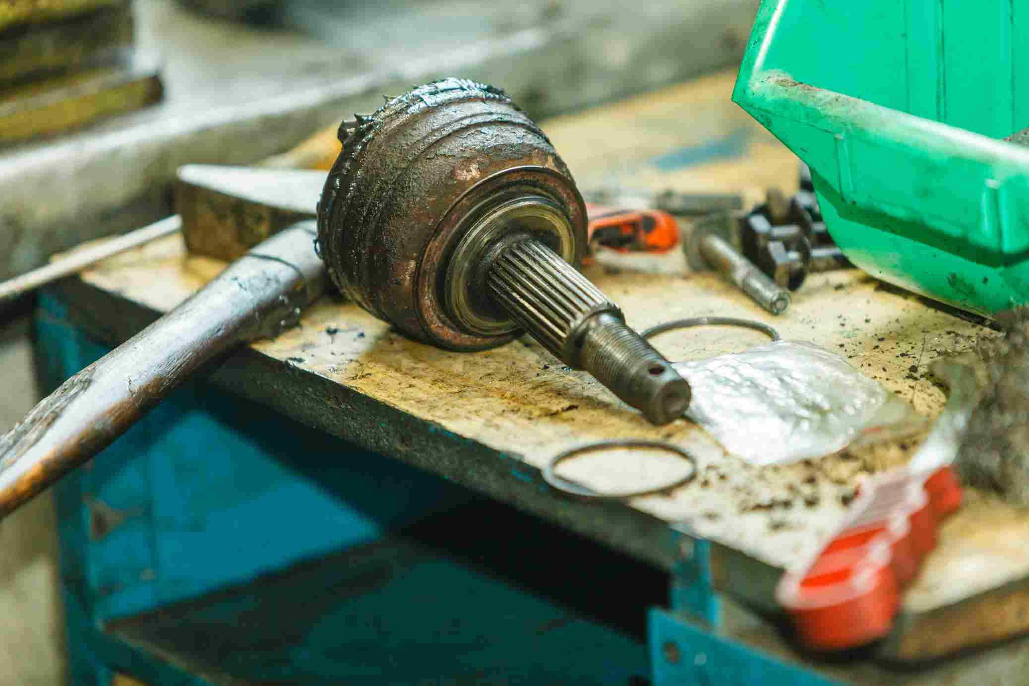 Greasy CV joint and axle shaft on a cluttered workbench with tools and parts