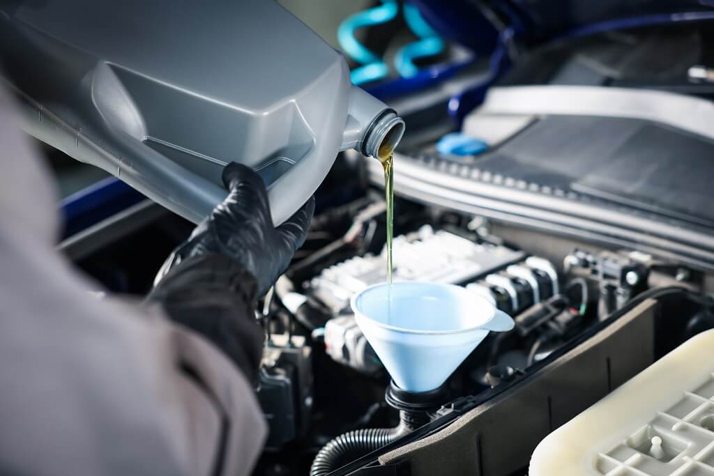 Mechanic pouring engine oil into Ford F-150 engine using funnel during maintenance