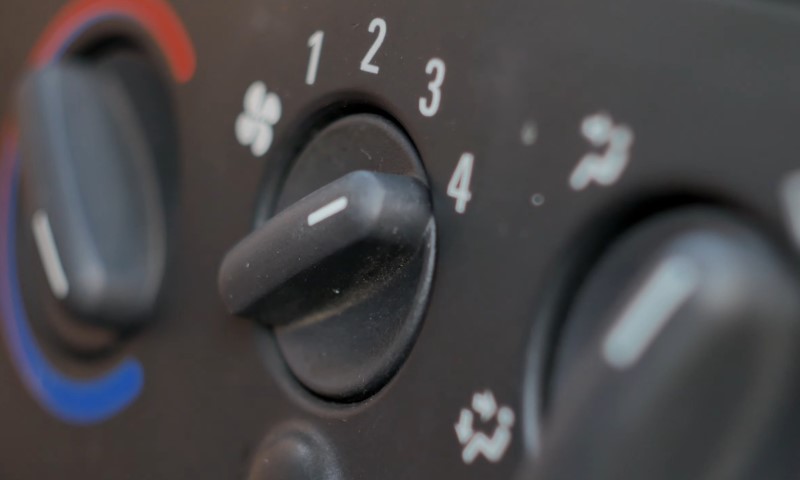 Close-up of a car's climate control knobs. Central knob set to 3, surrounded by fan and air direction symbols. Blue and red arcs indicate temperature control